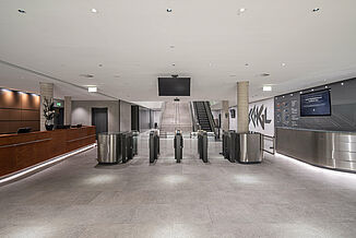 Eingangsbereich mit gefliestem Fußboden, Rezeption und Treppenhaus mit Rolltreppe in der Silvretta Therme in Ischgl.