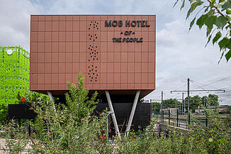 Braunes Gebäude mit der Aufschrift MOB Hotel, neben dem sich eine Bahnstrecke befindet